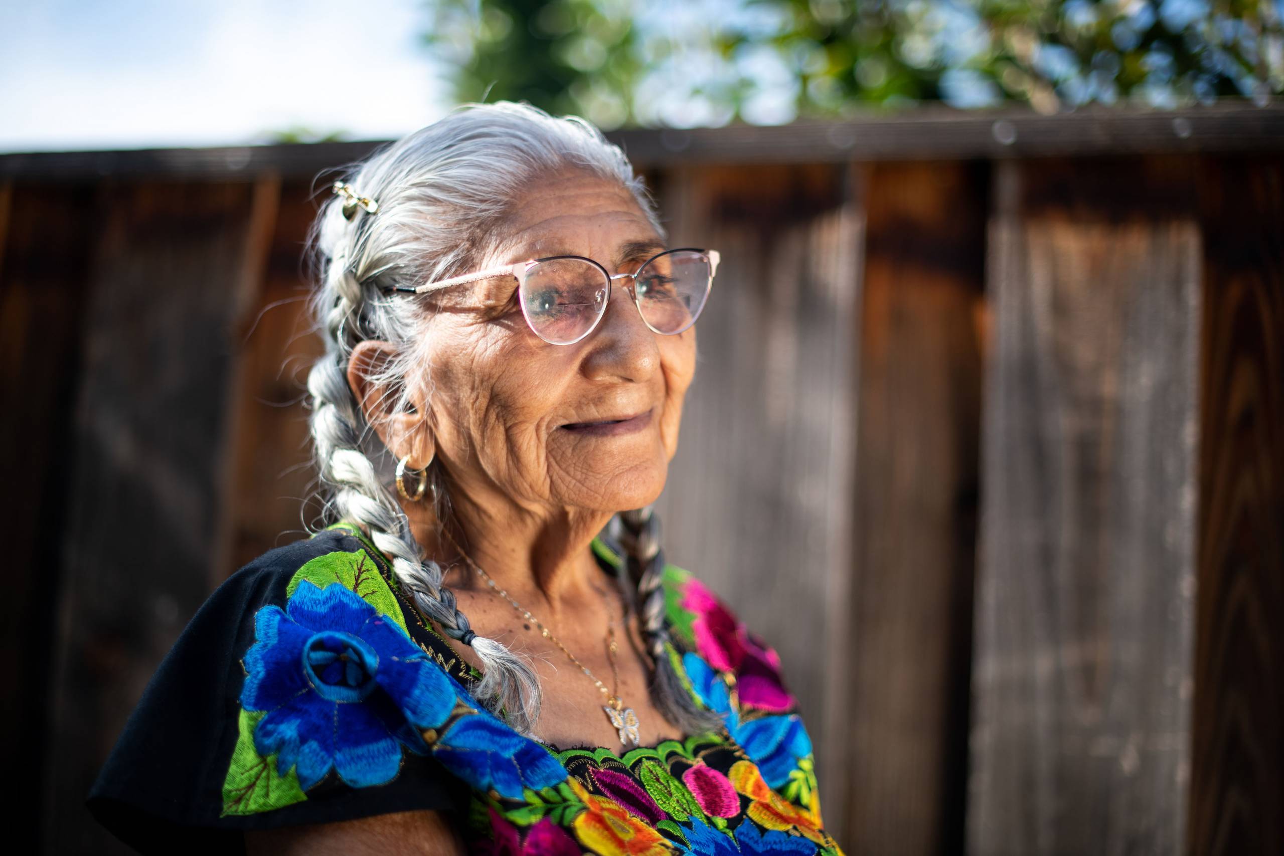 An elderly woman with glasses looks off into the distance.