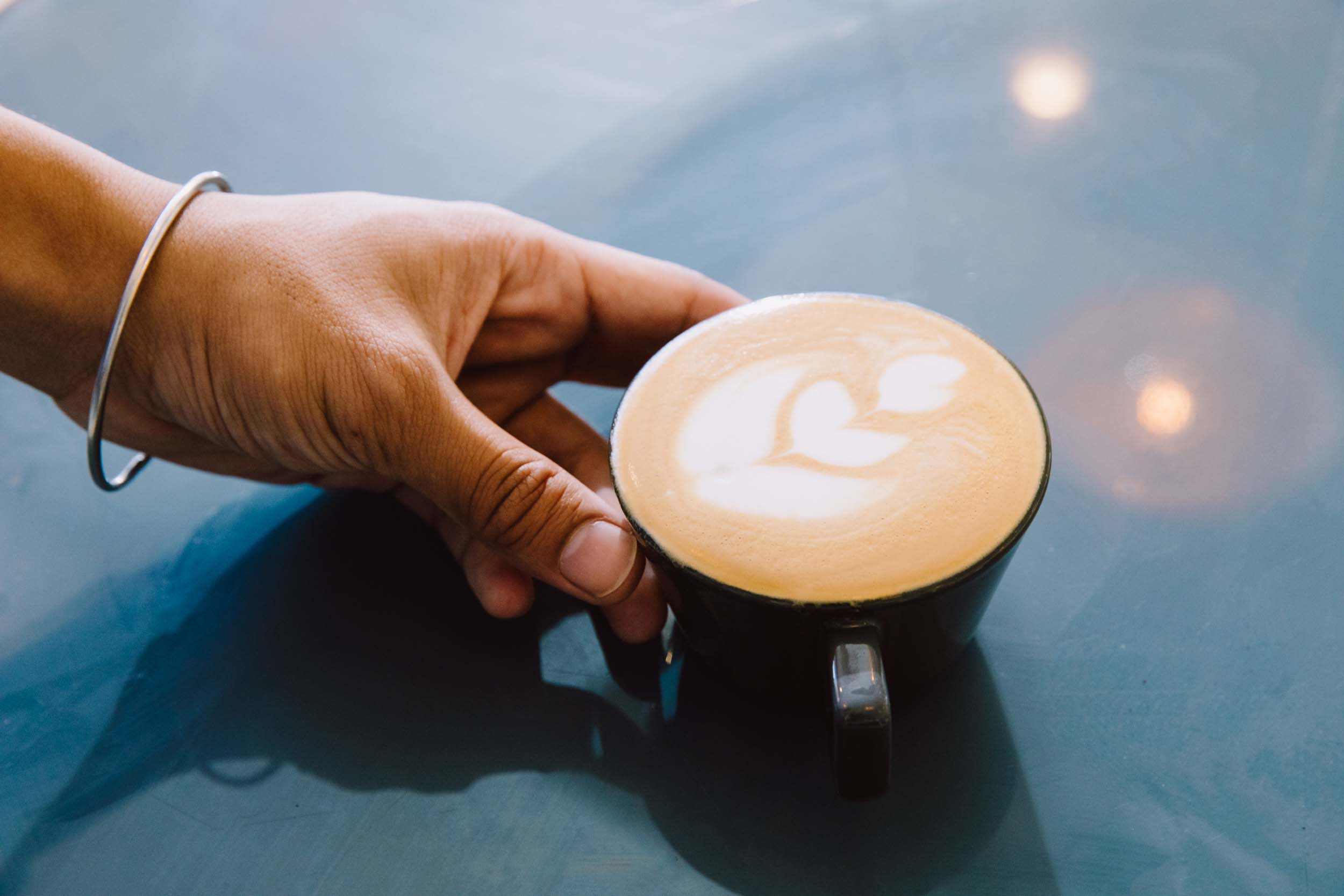 A hand reaching out to a cup of coffee decorated with elegant latte art.