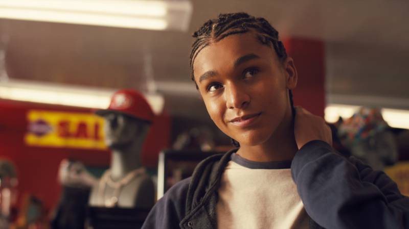 A Black teenage boy with cornrows looks up, half-smiling.