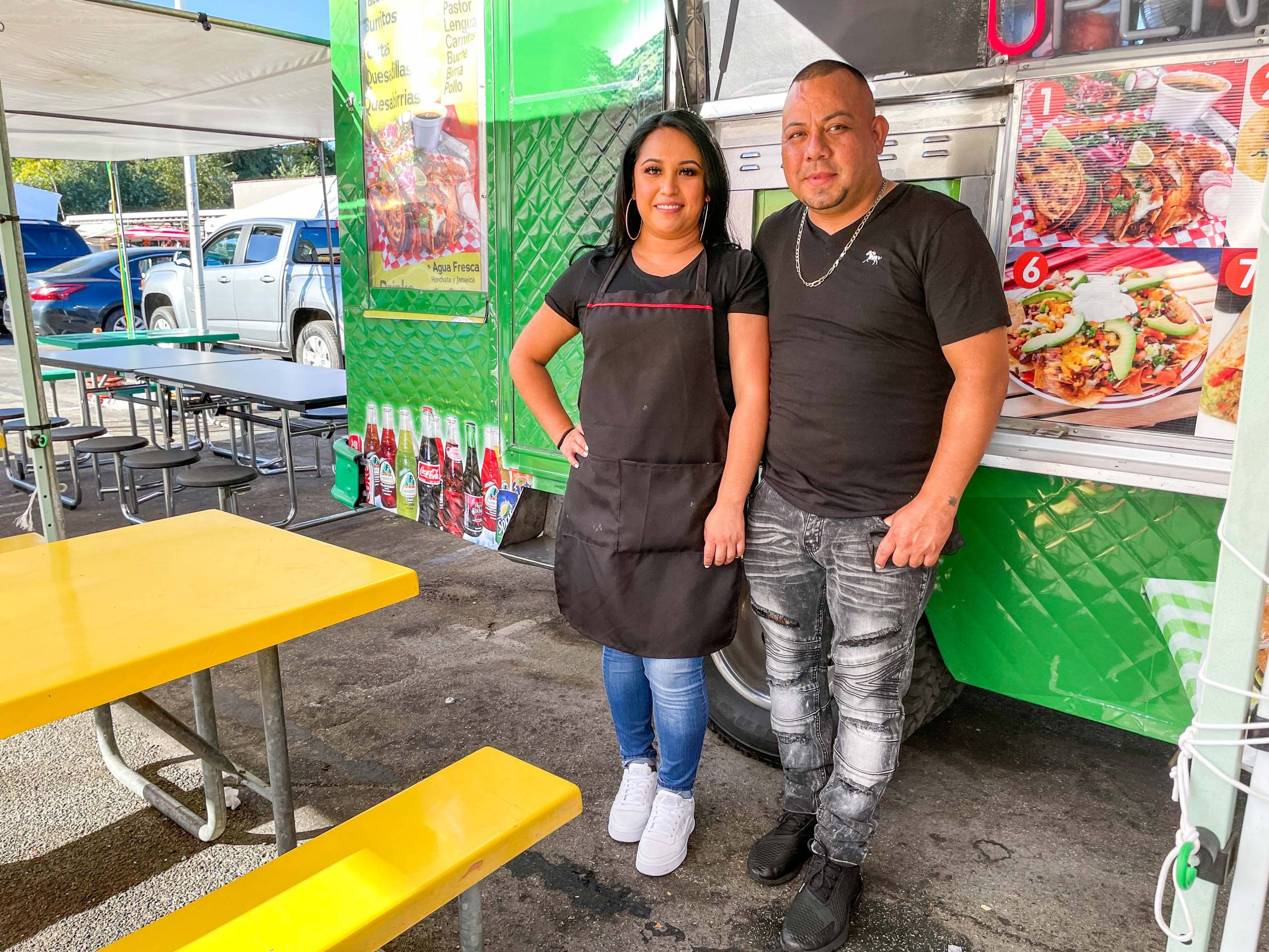A man and woman stand in front of a green taco truck.