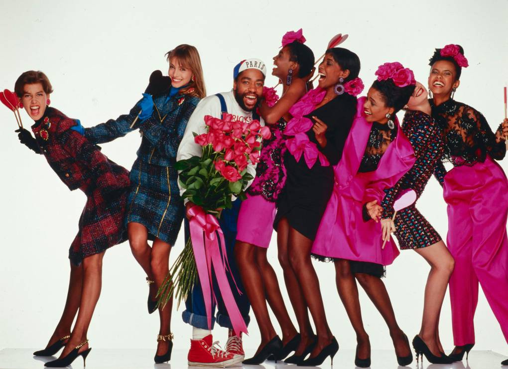 Models in bright pink clothes surround Patrick Kelly.