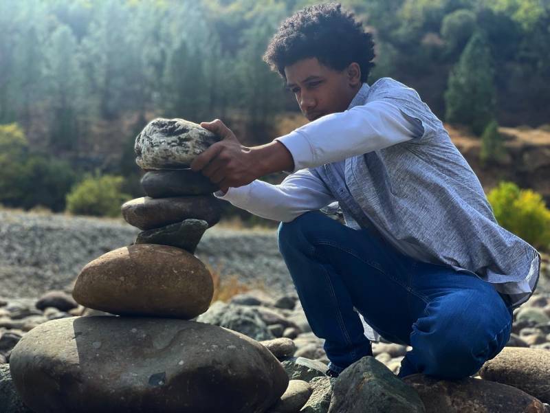 A young man stacks rocks in a riverbed