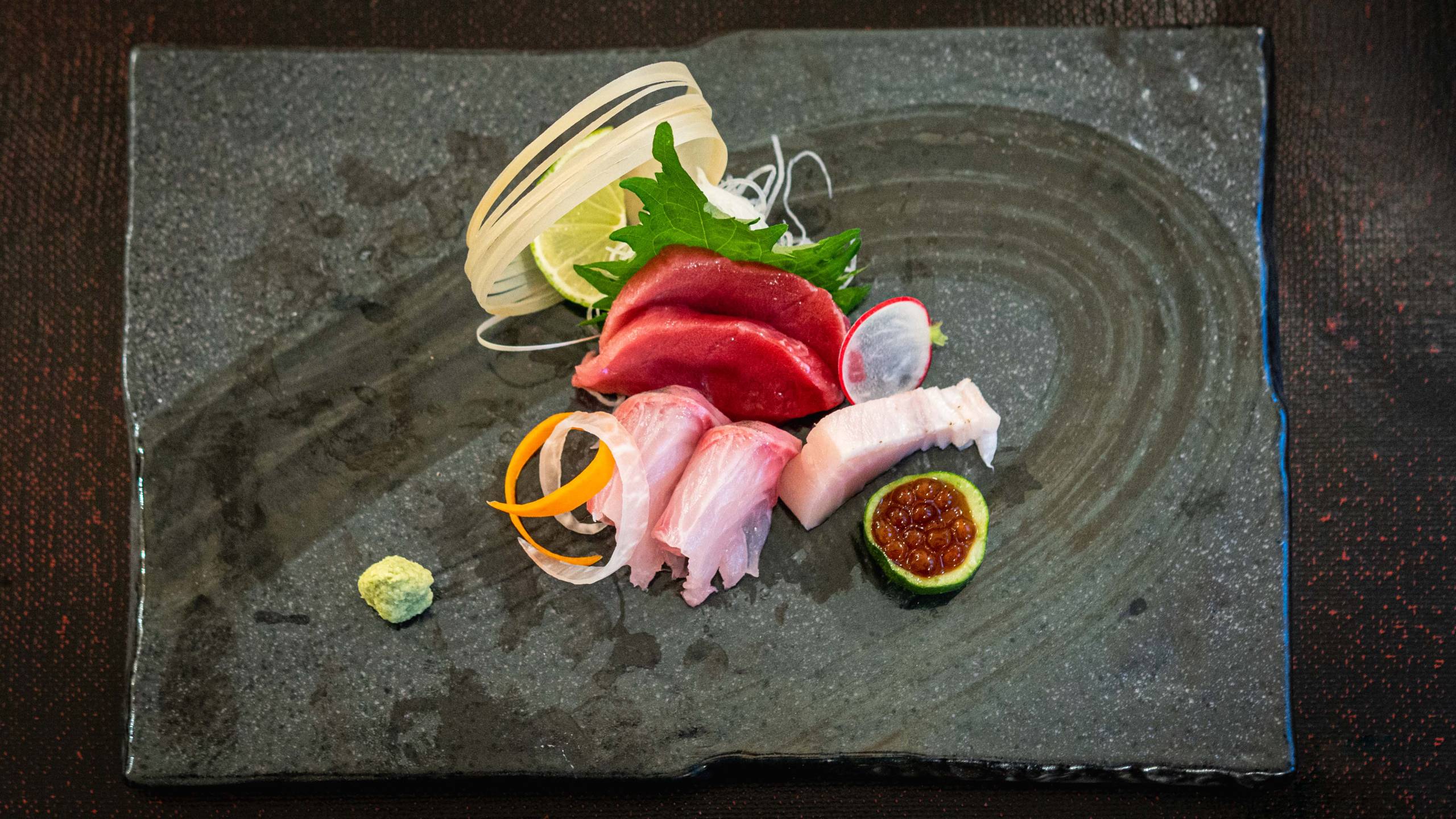 Artfully arranged sashimi on a dark gray serving tray.
