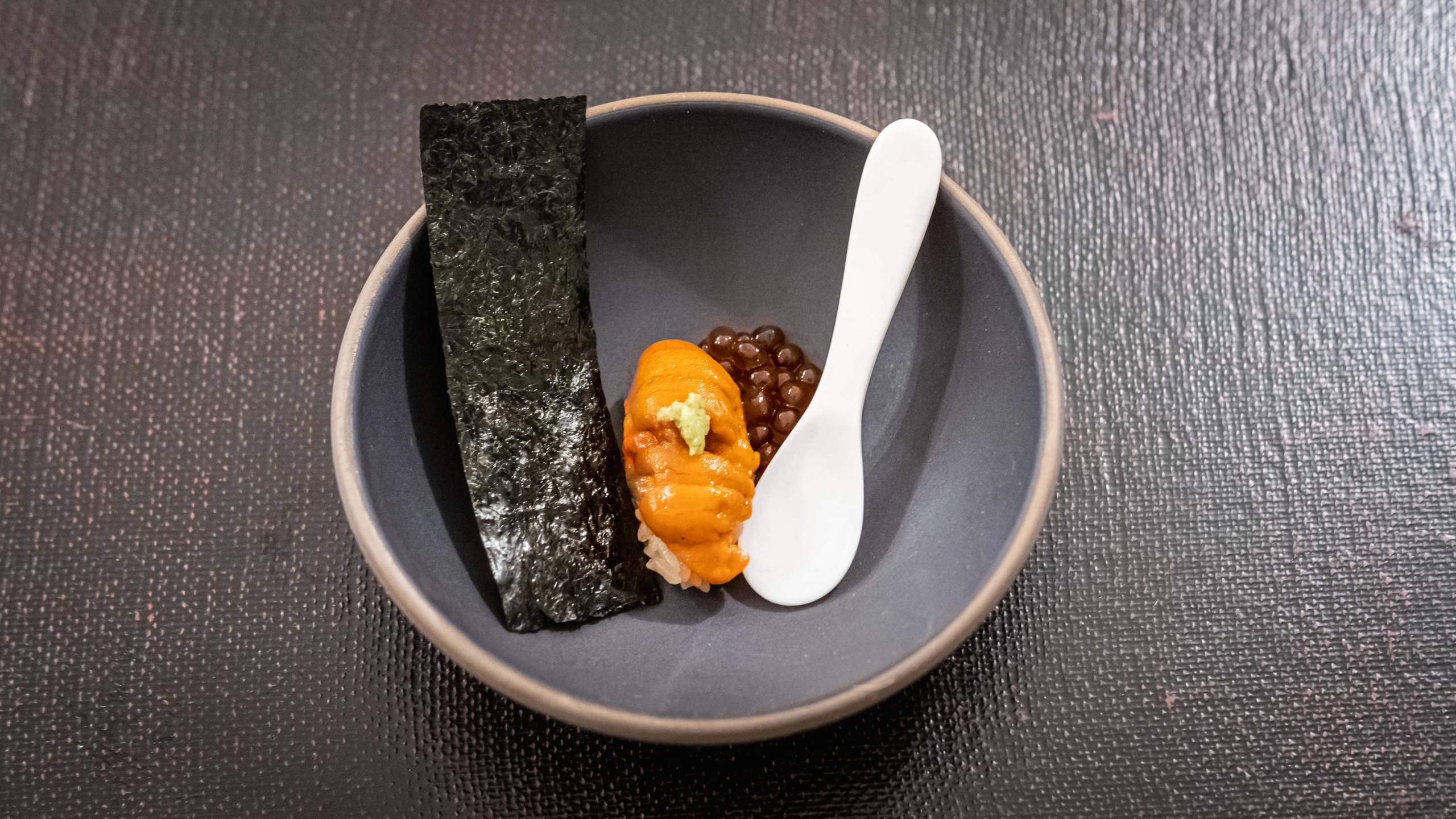 Bright orange uni nigiri served in a bowl with toasted seaweed and salmon roe.