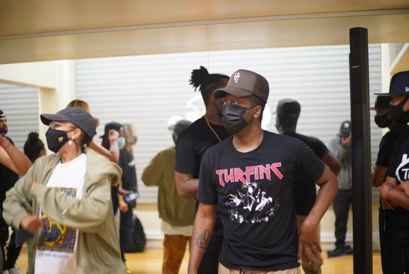 Tarik Rollerson wears a black mask, a black and grey hat and a shirt that reads "Turfin" on it as he leads a dance lab session at In The Groove Studios.