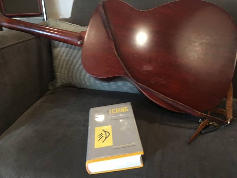 A copy of the I Ching sits on a sofa next to an acoustic guitar.