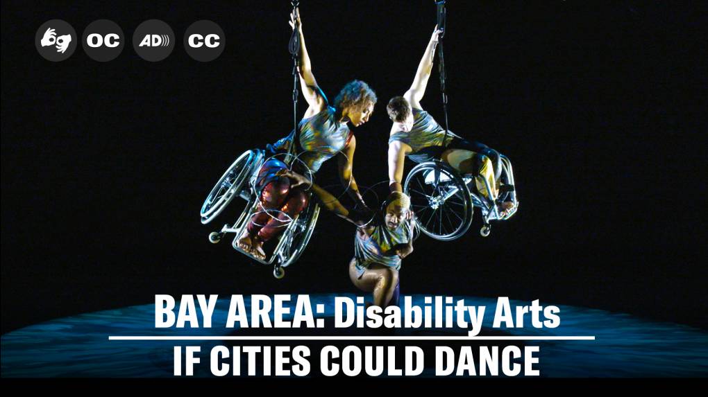 A wide shot of three dancers on a dimly lit stage; the floor is awash in patterned green and blue light. Two dancers in wheelchairs hover above the ground, each with one arm extended up, holding on to a thick cable; Alice is a multiracial Black woman with coffee-colored skin and short curly hair and Laurel is a white woman with very short cropped hair. They each gaze at and tilt down toward Jerron, a dark-skinned Black man with blonde hair who is crouched between them, wrapped in barbed wire. All dancers are wearing shimmery green and gold costumes.