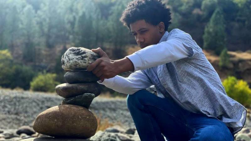 A young man stacks rocks in a riverbed