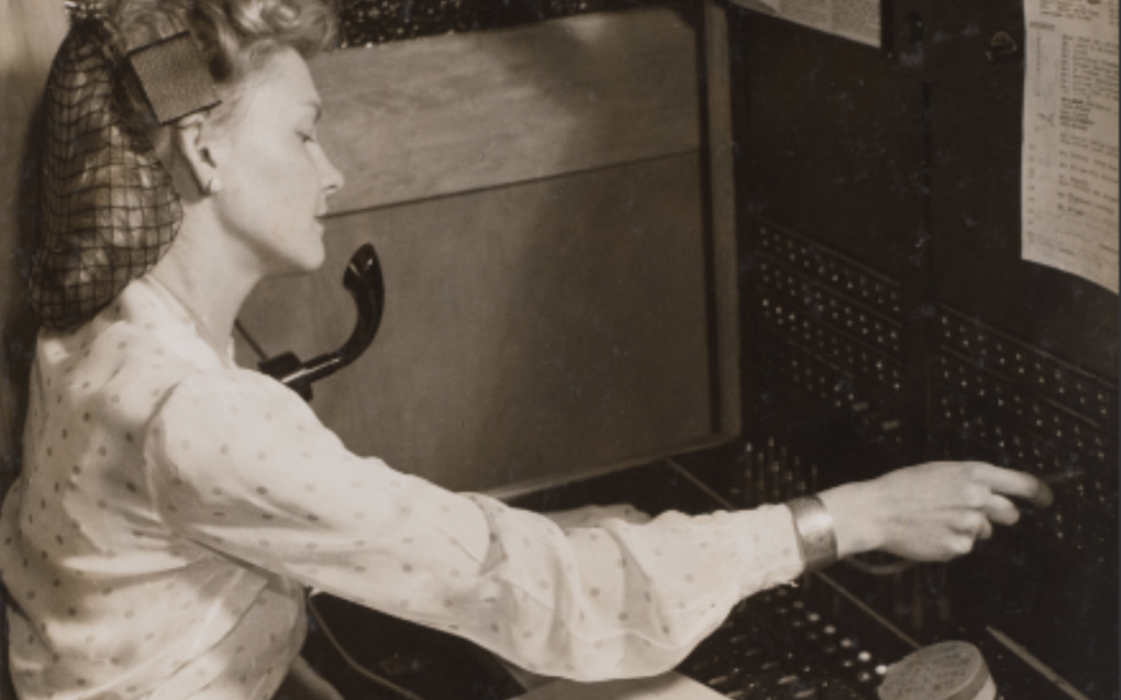 Woman wearing a hairnet operates a switchboard in early 1940s New York.