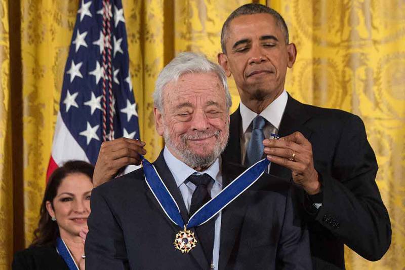 The president places a gold medal around the neck of Stephen Sondheim.