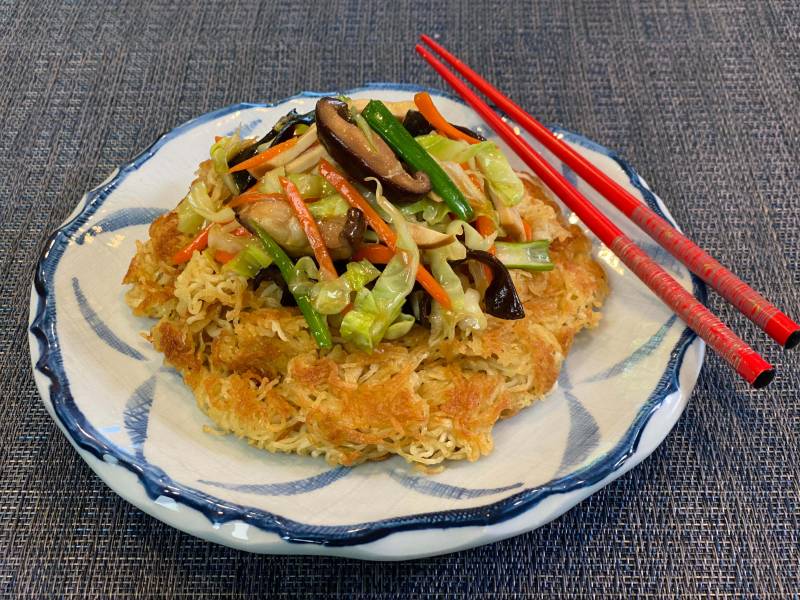 Stir-fried vegetables on top of a crispy noodle pancake, with a pair of red chopsticks.