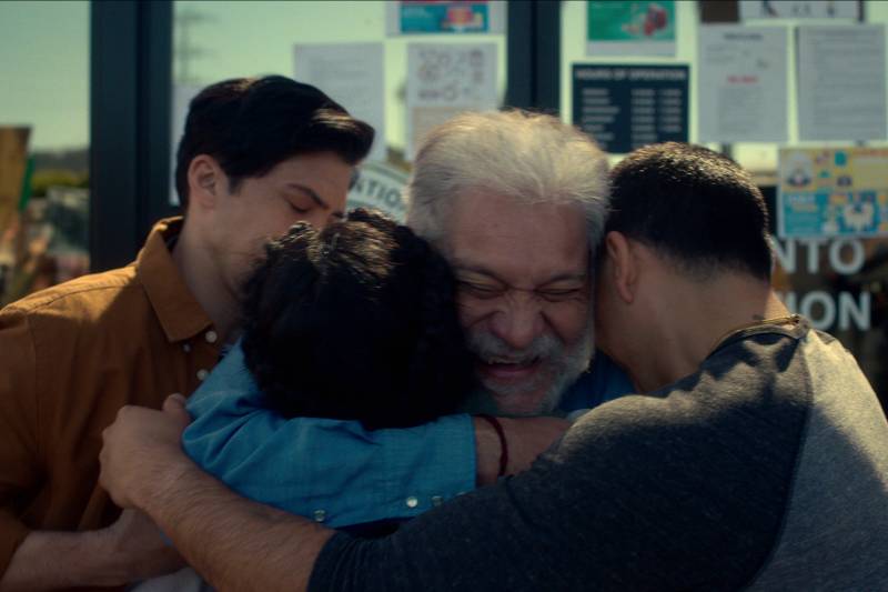 An older Latino man smiles broadly as he is embraced by three younger people.