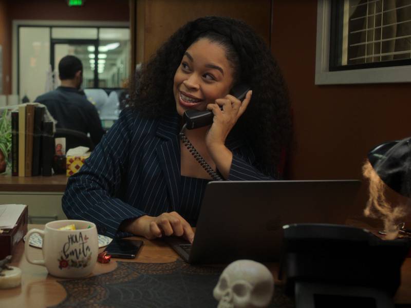 An Afro-Latina woman sits behind a computer, happily talking on the phone in an office.