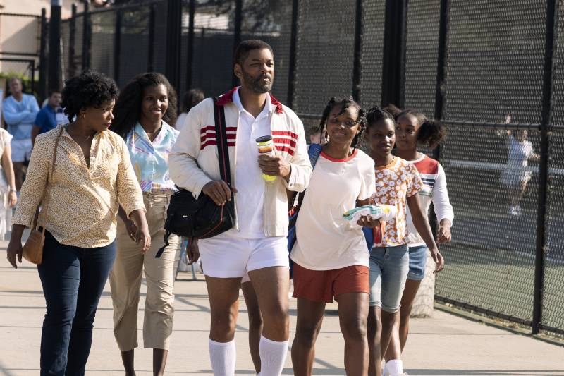 A still from the film ‘King Richard’ depicting parents Richard and Oracene walking past a tennis court with four of their daughters.