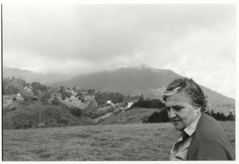 Black-and-white image of an older woman in front of foggy landscape.