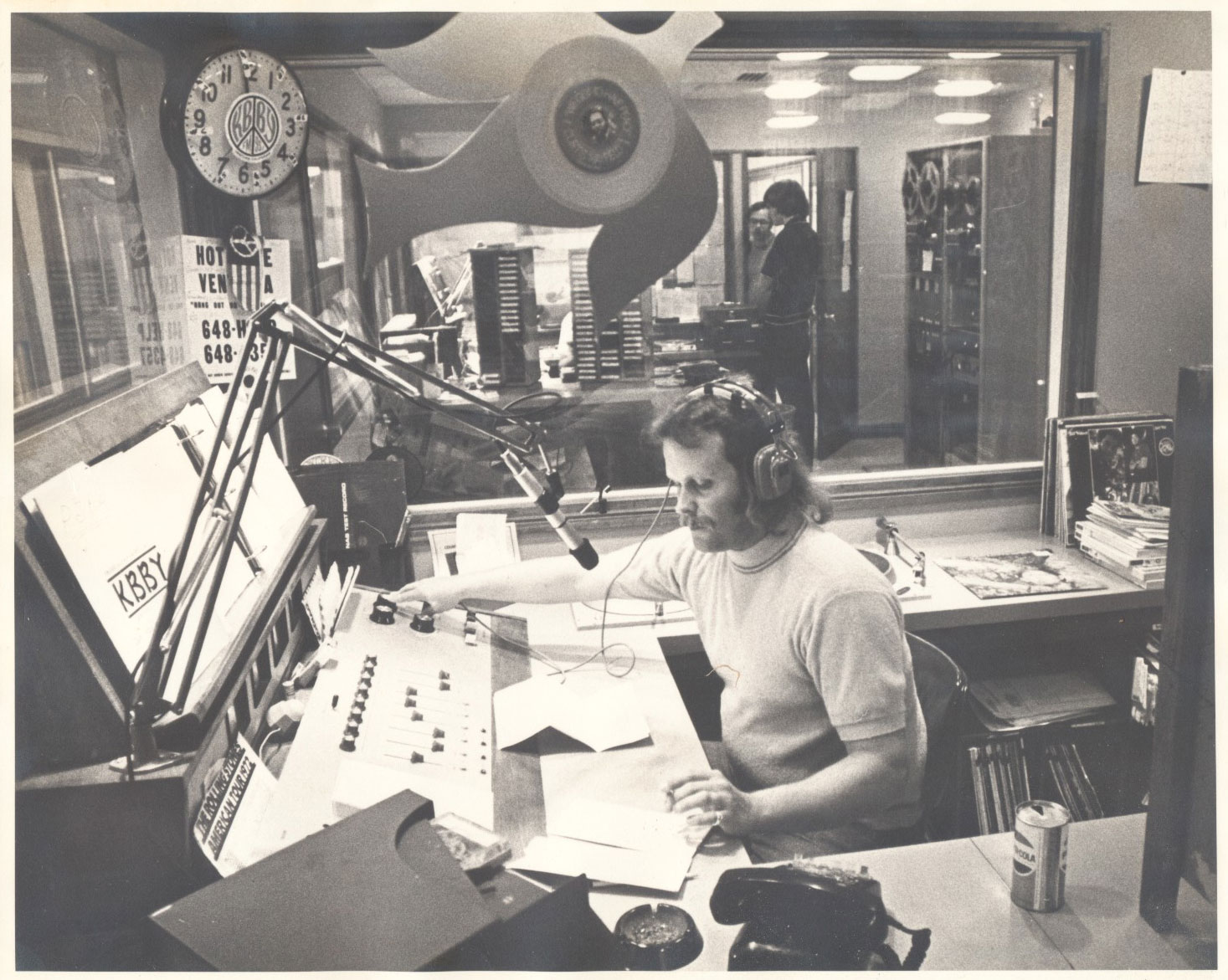 A young Bill Bowker sits in a radio booth, cigarette in hand.