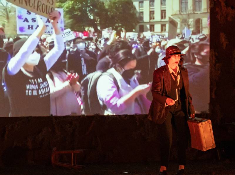 Woman stands on stage in front of projected image of Black Lives Matter march.