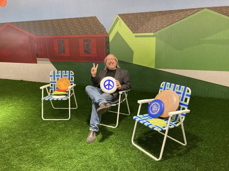 A white middle aged man sits in lawn chair surrounded by a collection of frisbees.