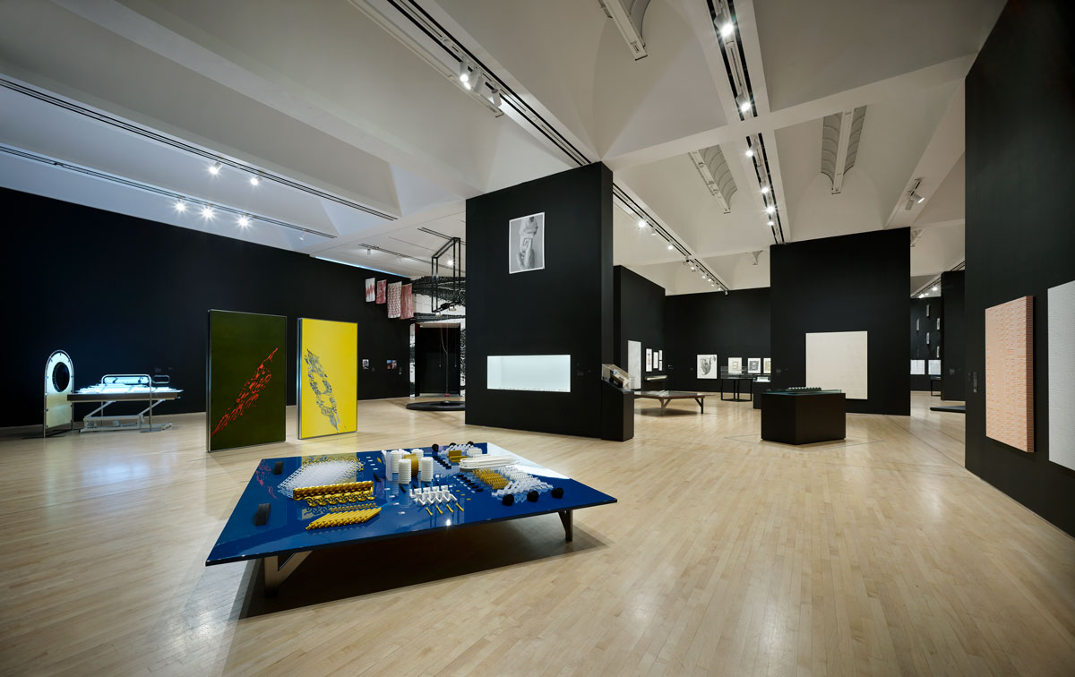 View of exhibition space with black walls, paintings and sculptures.