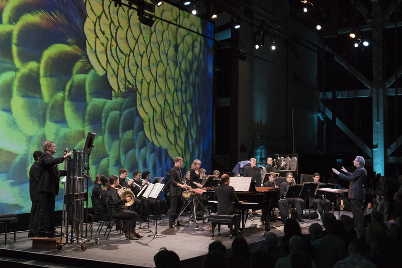 Orchestra musicians perform with a background of elaborate, colorful video projections.