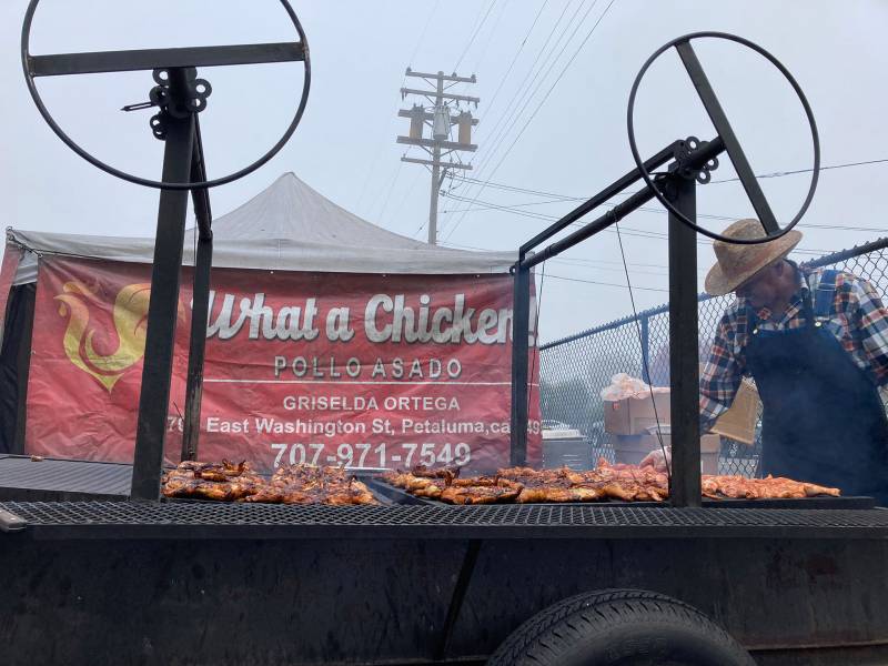 A man in a flannel and hat tends to chicken on a grill on an overcast day
