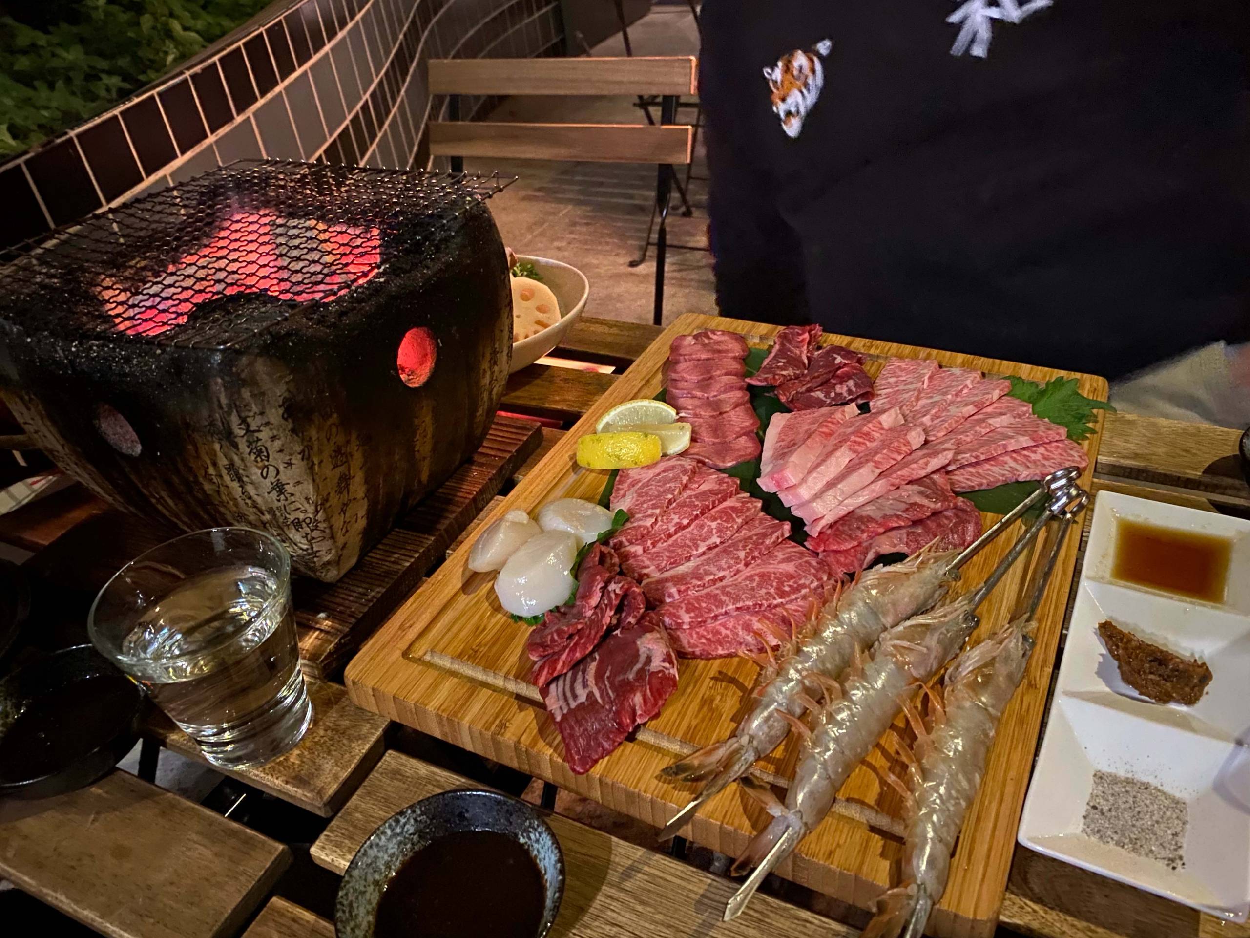A spread of raw meat and seafood next to a Japanese-style tabletop charcoal grill. 