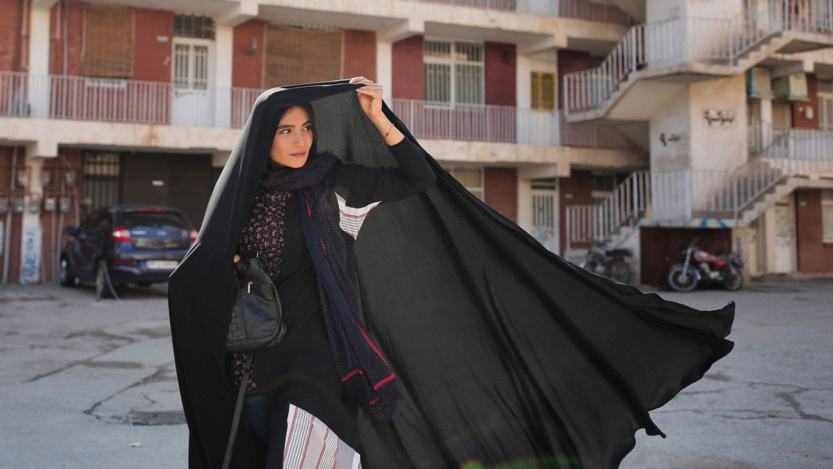 A woman lifts a black headscarf and looks to the right