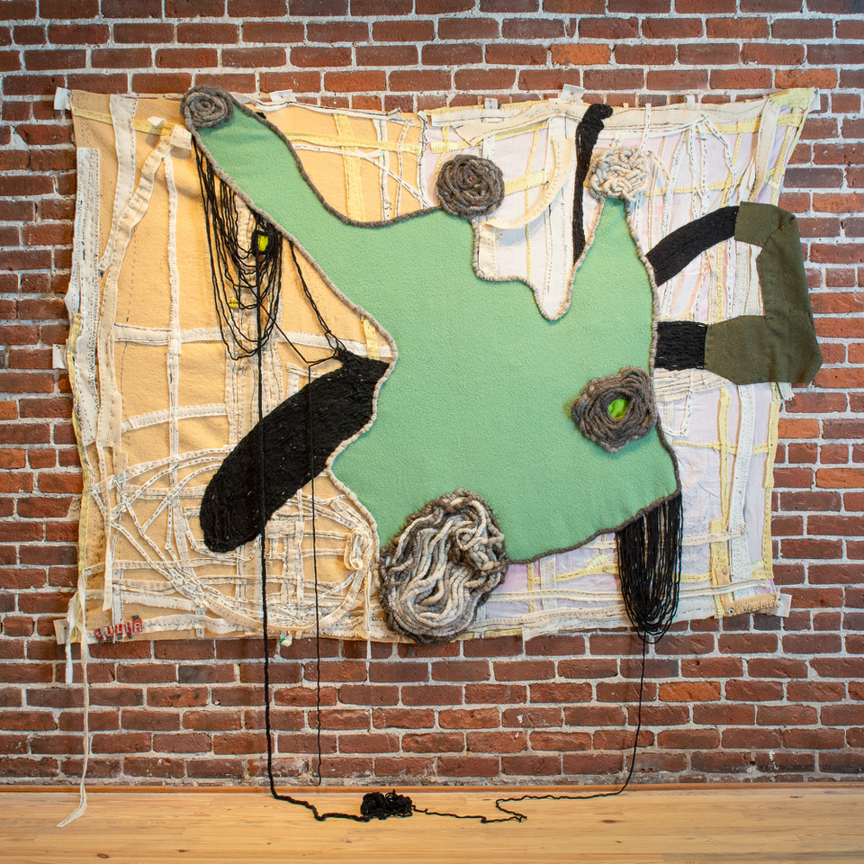 Textile piece against brick wall, light green, peach and white colors.