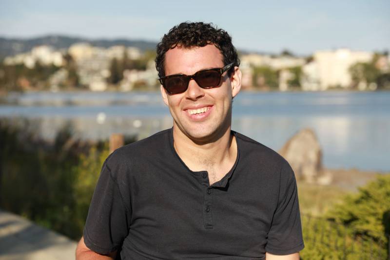 A light skinned man with sunglasses smiles.