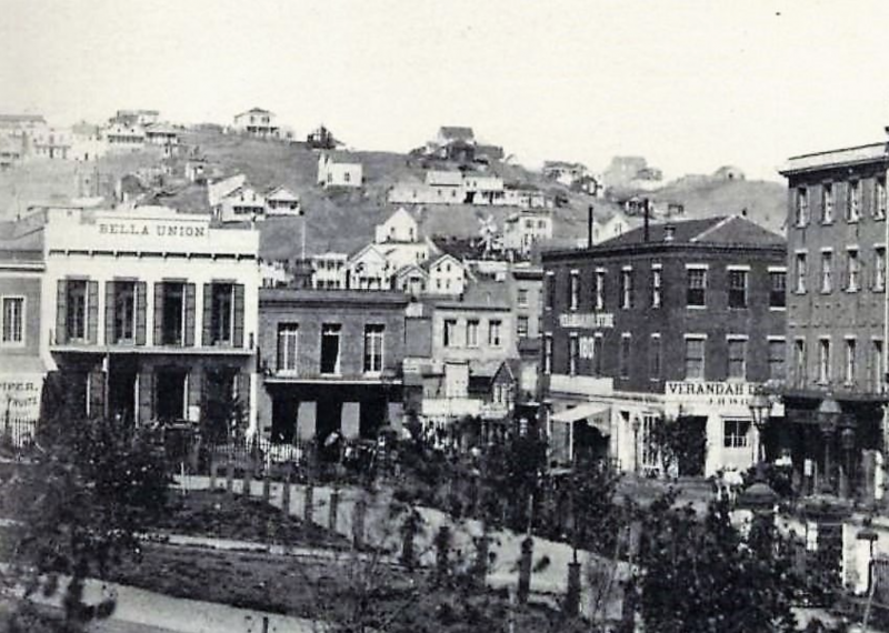 A row of Gold Rush era store fronts line a street with sparsely populated hills behind.