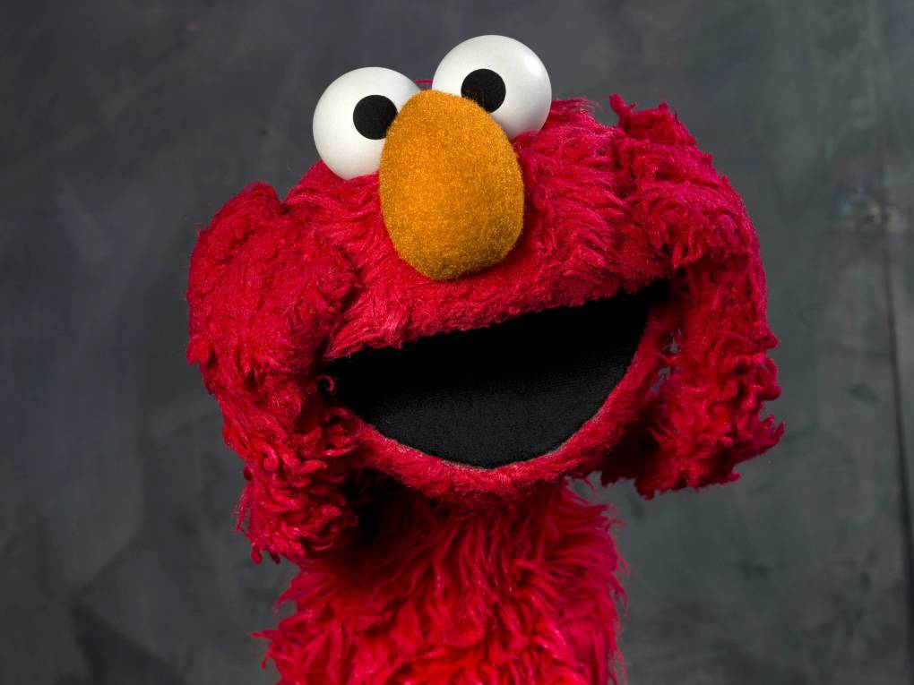 Elmo, the fuzzy red 'Sesame Street' puppet, poses with his mouth open and his hands holding either side of his face.