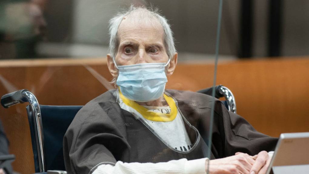 An elderly man with grey hair that's thin on top, sits wearing a surgical mask in court, looking disheveled.