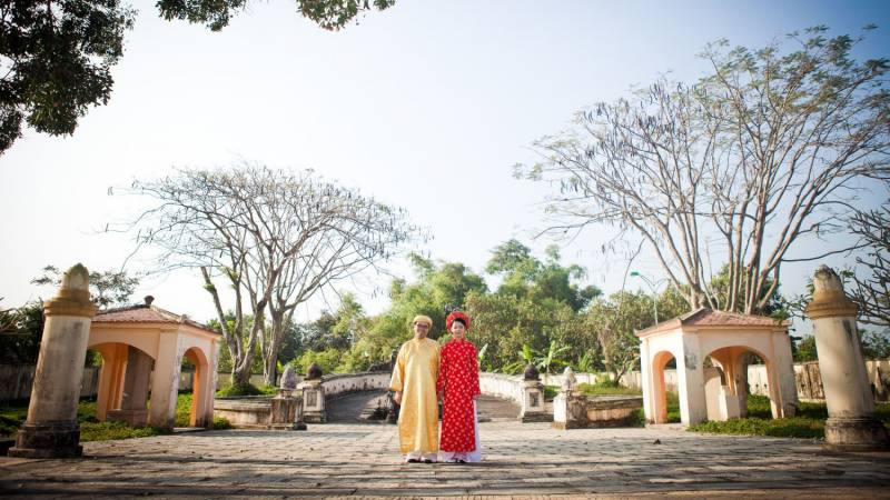A man and woman pose for a portrait wearing colorful ao dai.