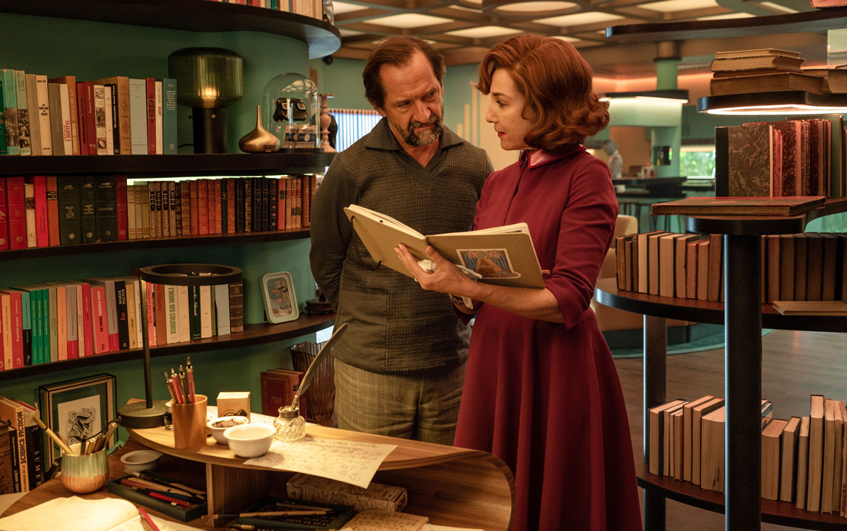 A man and a woman look at a book in a small library room