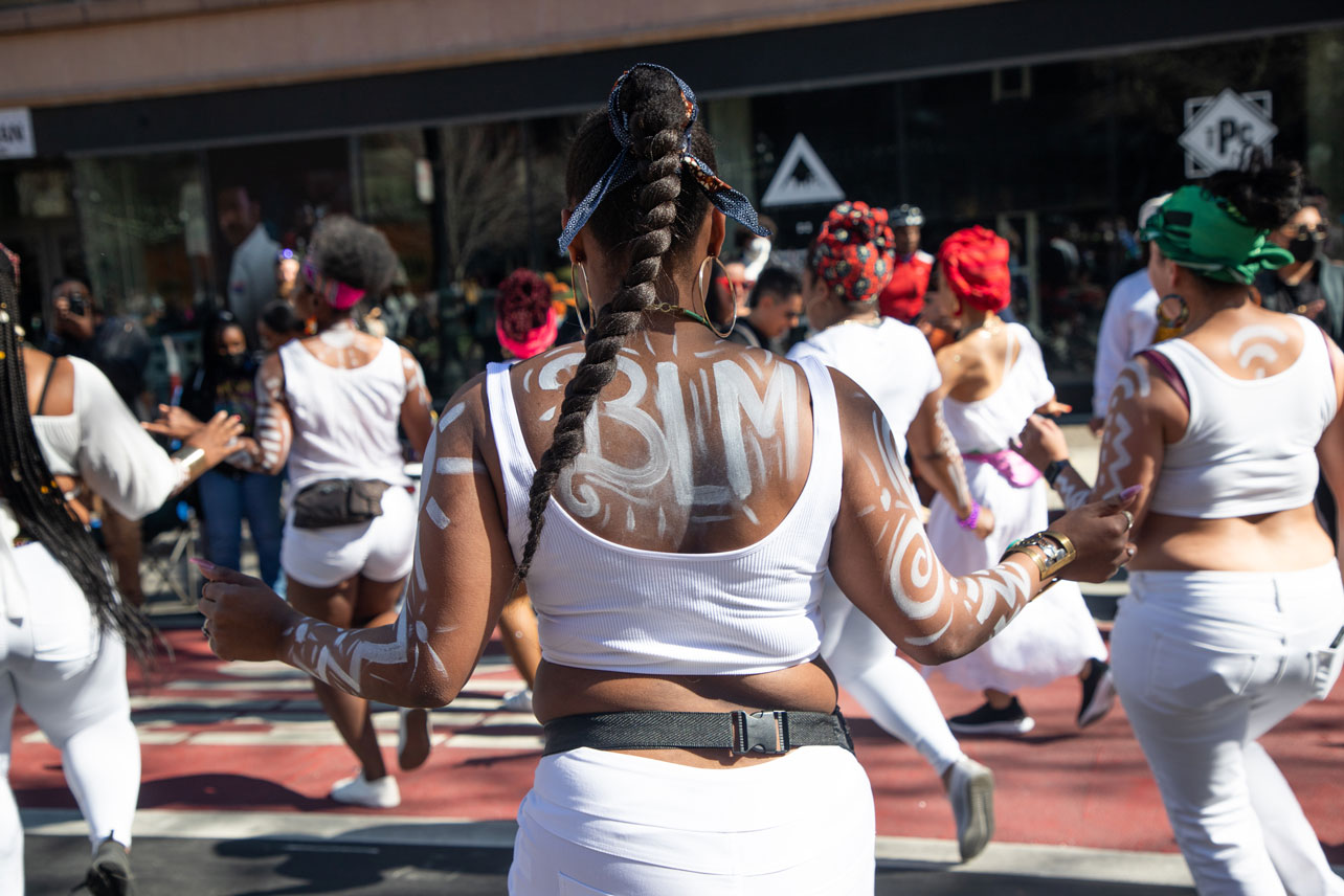 A dance group in white, one woman has "BLM" written on their back