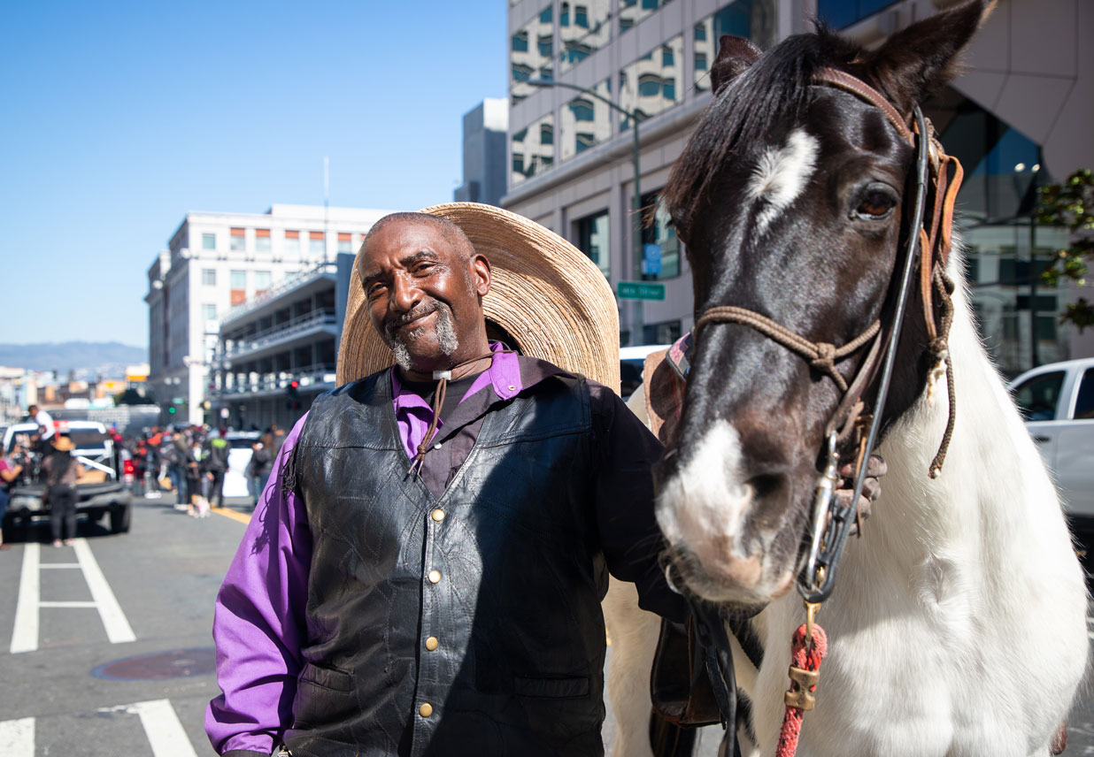 A person in a vest smiles next to a black and white horse