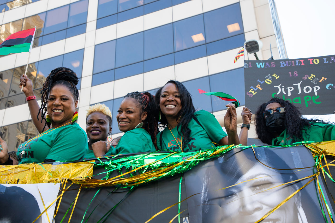 Five women in green shirts smile from a float