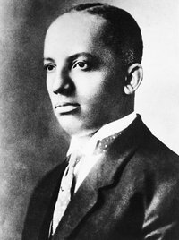 A black and white portrait of a young Black man wearing a smart suit jacket, tie and starched white shirt.