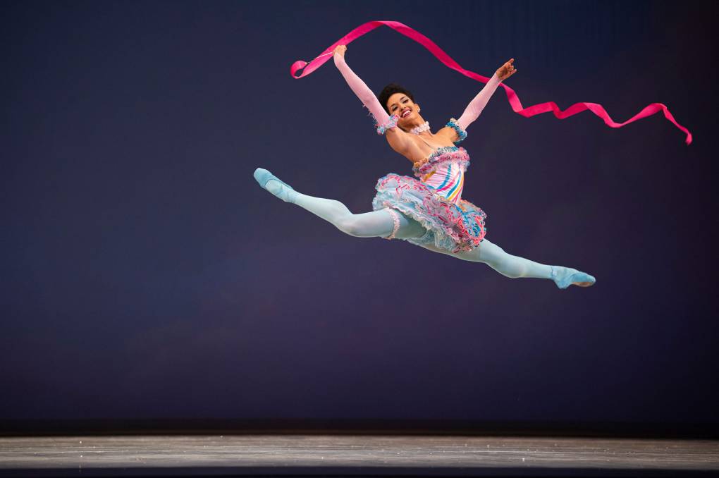 A dancer on stage leaps in the air with a red ribbon.