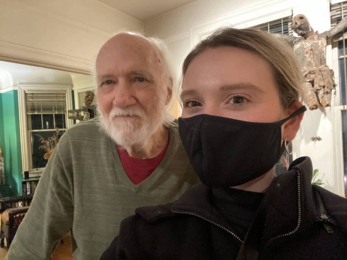 An older man and a younger woman in a face mask pose for camera