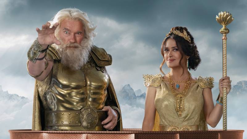An elderly man in a gold breastplate holds his hands out next to a younger woman similarly festooned in gold