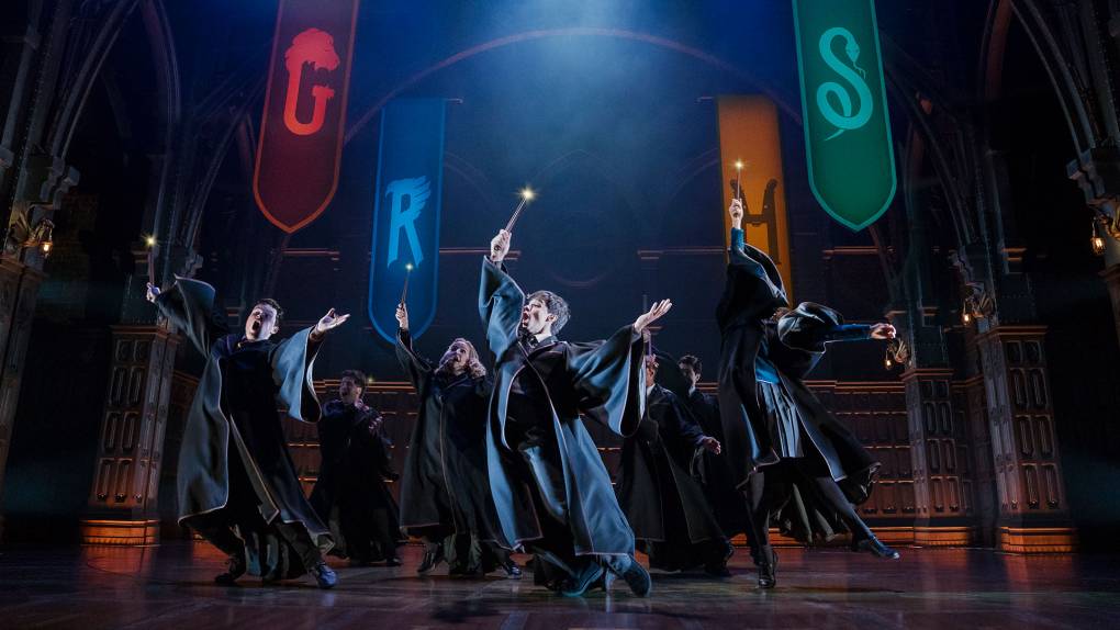 Four young boys in robes wave wands in the air, leaning leftward