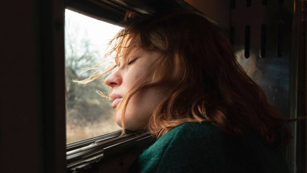 Woman with red hair puts face to train window with eyes closed
