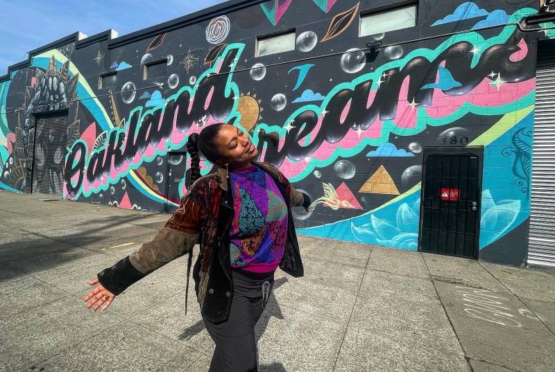 Filmmaker, poet and friend Nijla Mu'min poses for a photo in front of a mural that reads Oakland Dreams, by Trust Your Struggle. 