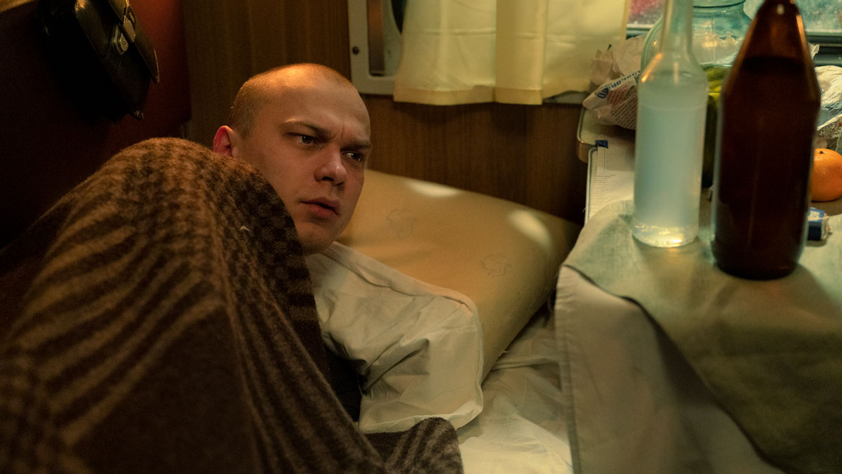 Man with shaved head looks up from train bed