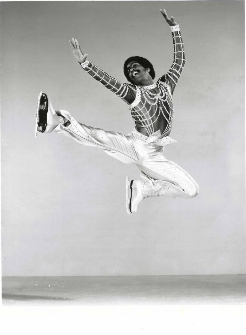 Atoy Wilson leaps several feet off the ice, reaching his arms up, with one leg fully extended and the other bent.