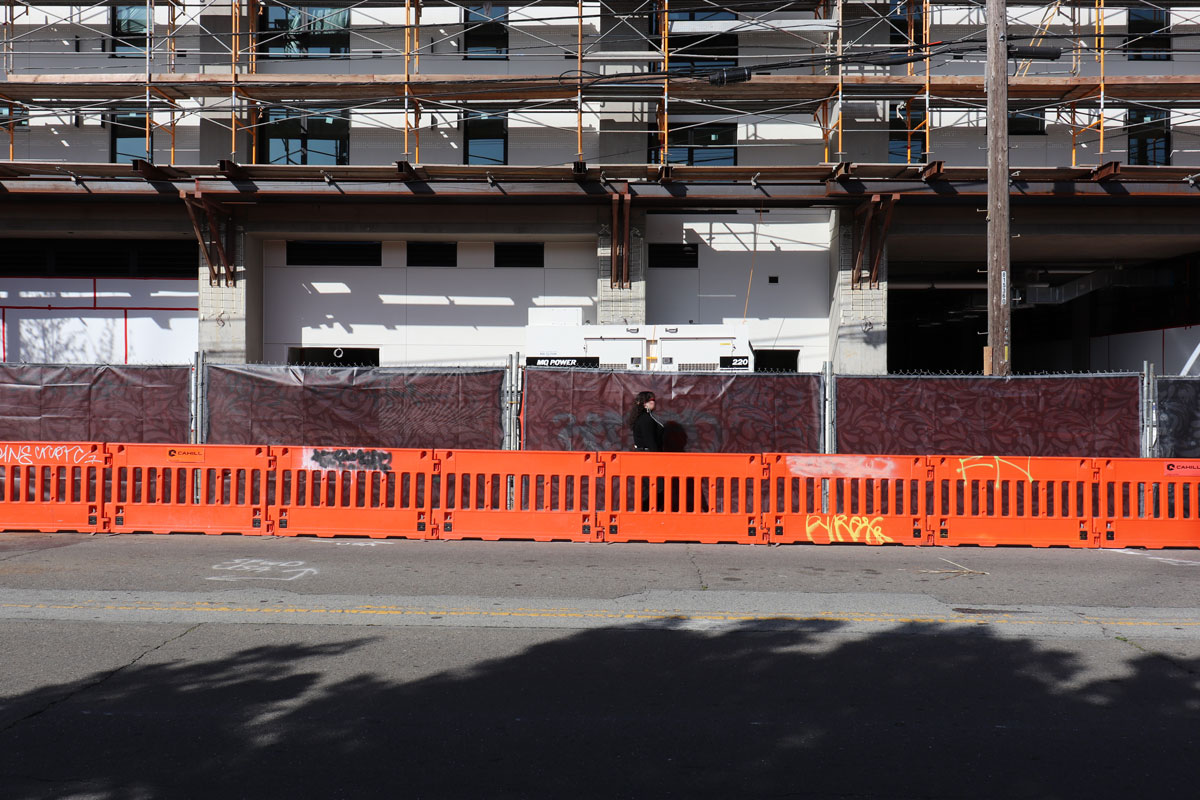 Woman walks behind orange barricades under scaffolding of building