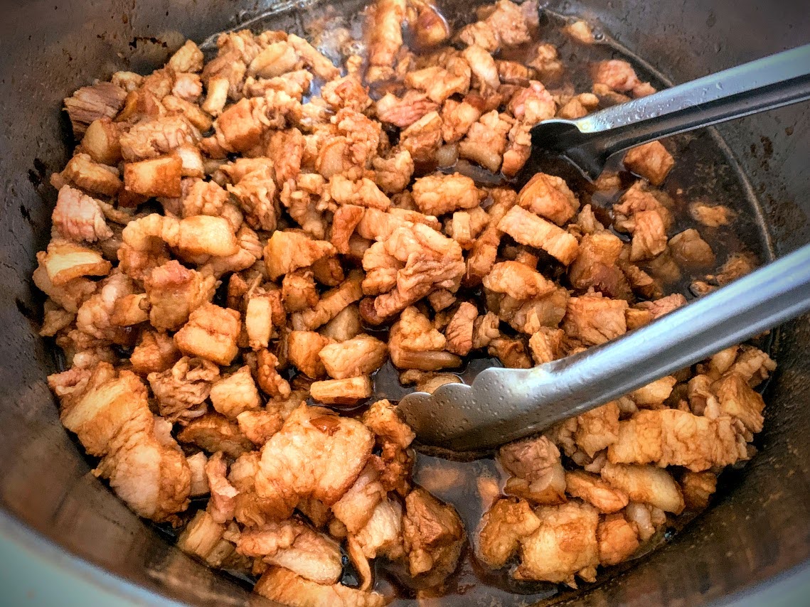 Pieces of hand-cut pork belly simmering in the pan.