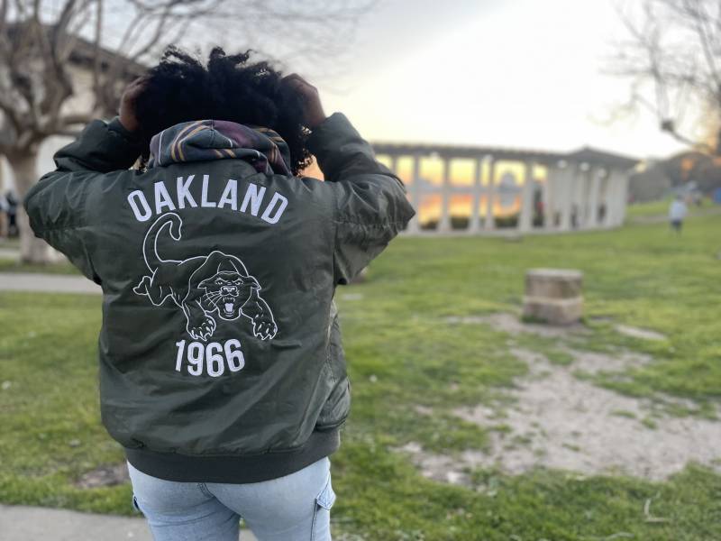 Artist, educator and friend Venus Morris stands by Lake Merritt at sunset while wearing a jacket with the logo of the Black Panther Party, made by MADOW FUTUR. 
