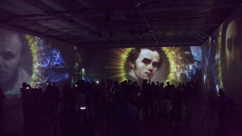 Projected images of paintings in a dark, crowded room